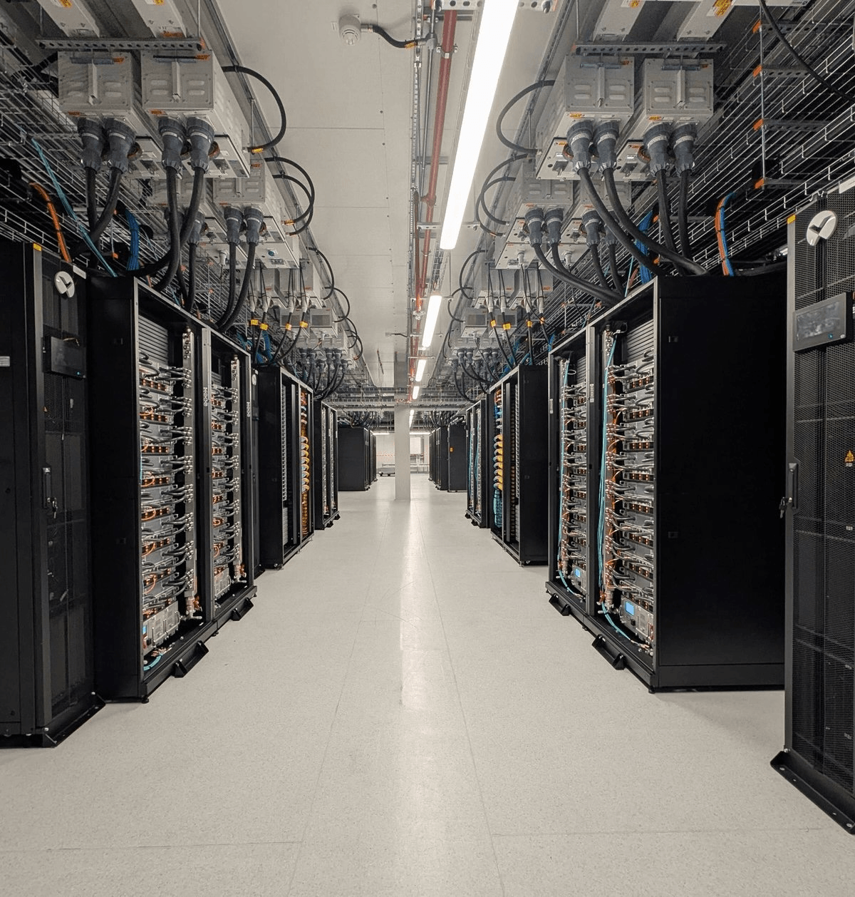 Server-room aisle between rows of black racks, with overhead cabling, fading into charcoal.